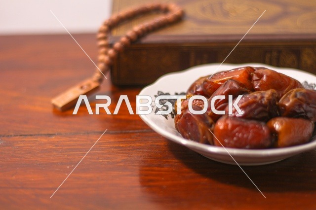 تمر رمضان مع المصحف والمسبحة على طاولة خشبية