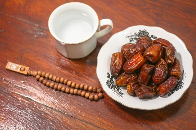 تمر رمضان وكوب ماء مع مسبحة على خشب