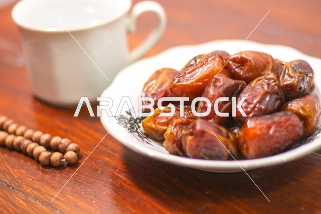 طبق تمر مع سبحة صلاة على طاولة خشبية فى اجواء رمضانية