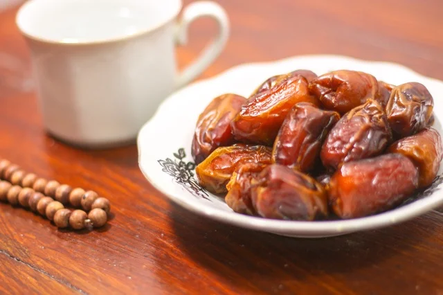 طبق تمر مع سبحة صلاة على طاولة خشبية فى اجواء رمضانية