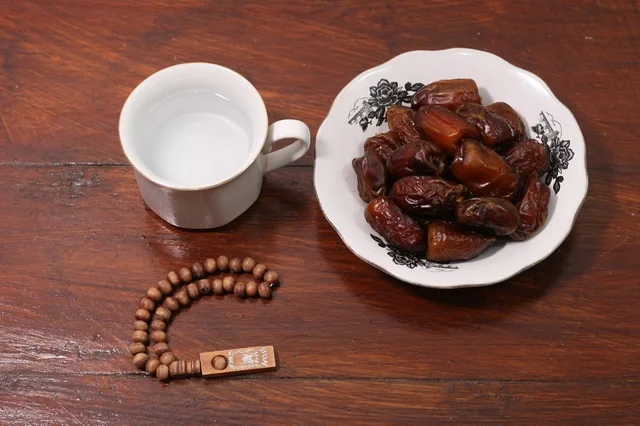 Ramadan dates and a glass of water with a wooden prayer bead in a Ramadan atmosphere.