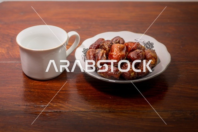 تمر مجفف في طبق مع كوب أبيض على طاولة خشبية لافطار رمضان
