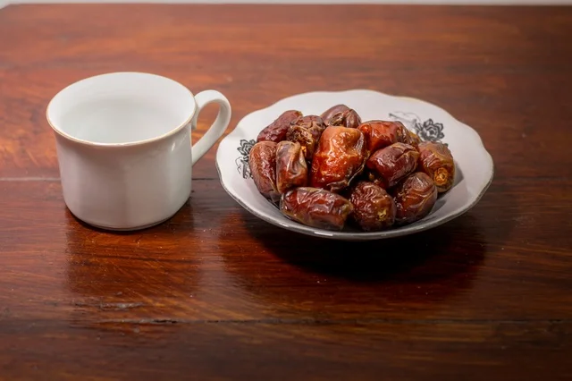 تمر مجفف في طبق مع كوب أبيض على طاولة خشبية لافطار رمضان