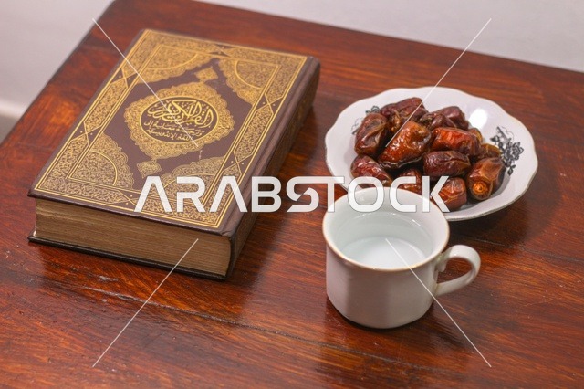 مصحف مع تمر وكوب ماء على طاولة خشبية لافطار رمضان