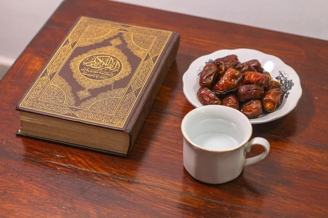 مصحف مع تمر وكوب ماء على طاولة خشبية لافطار رمضان