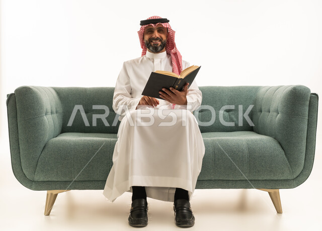 Saudi Man in Traditional Attire Reading Book on Sofa