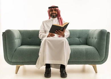 Saudi Man in Traditional Attire Reading Book on Sofa