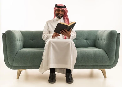 Saudi Man in Thobe Reading Book on Green Sofa