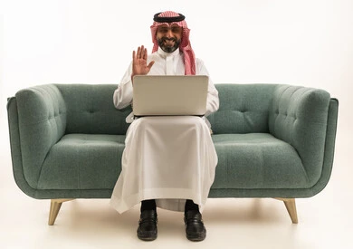 Saudi Man with Laptop on Green Sofa Waving
