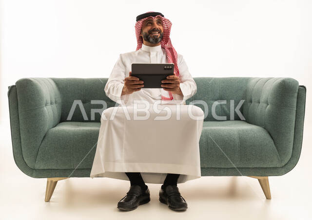 رجل سعودي مع جهاز لوحي على أريكة خضراء