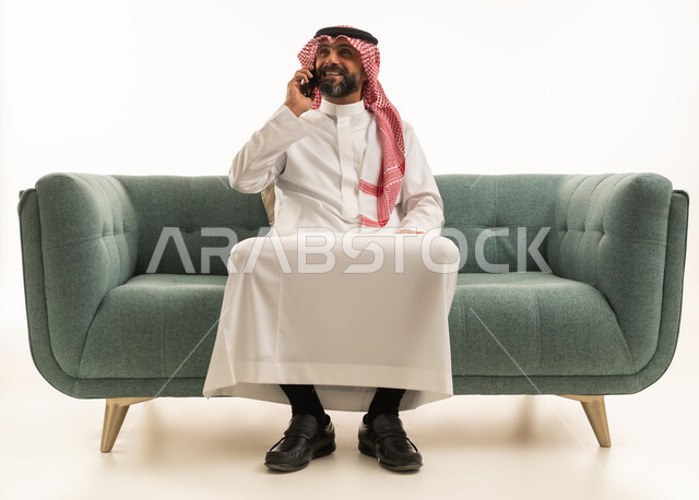 Saudi Man in Traditional Thobe Talking on Phone on Sofa