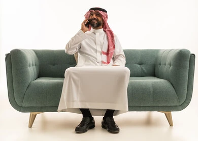 Saudi Man in Traditional Thobe Talking on Phone on Sofa