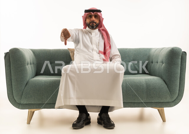 Saudi Man Giving Thumbs Down Gesture on Green Sofa