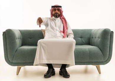 Saudi Man Giving Thumbs Down Gesture on Green Sofa