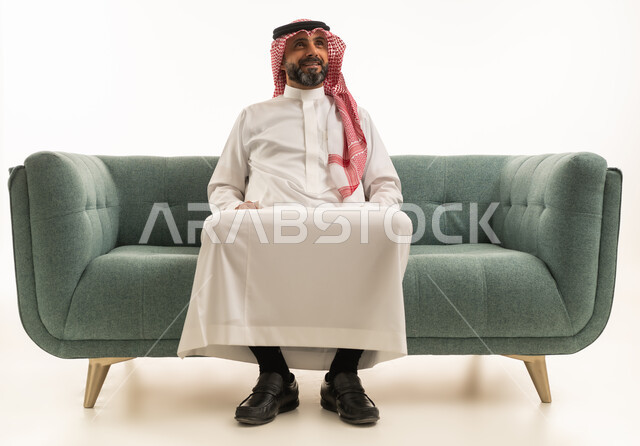 رجل سعودي بالزي التقليدي يجلس على أريكة خضراء