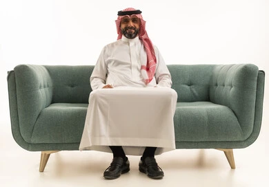 Smiling Saudi Man in Traditional Thobe on Green Sofa