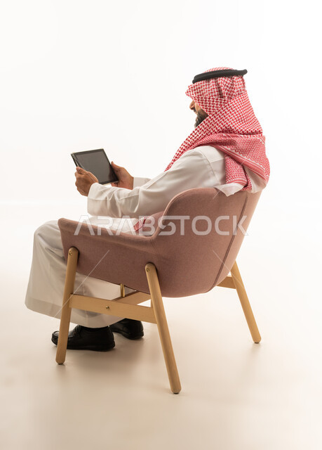 رجل سعودي بالزي التقليدي يستخدم جهاز لوحي بخلفية بيضاء