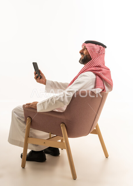 رجل سعودي بالثوب التقليدي يجلس مع هاتف ذكي