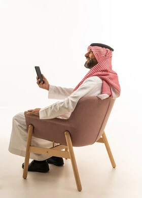 رجل سعودي بالثوب التقليدي يجلس مع هاتف ذكي
