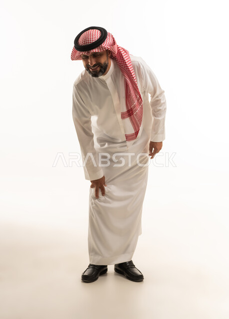 رجل سعودي بالثوب التقليدي ينحني على خلفية بيضاء