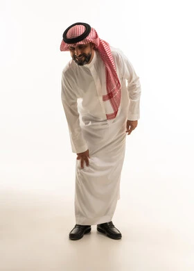 رجل سعودي بالثوب التقليدي ينحني على خلفية بيضاء