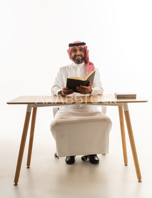 Saudi Man in Traditional Thobe Reading at Desk
