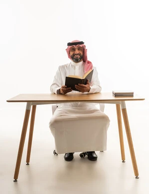 Saudi Man in Traditional Thobe Reading at Desk
