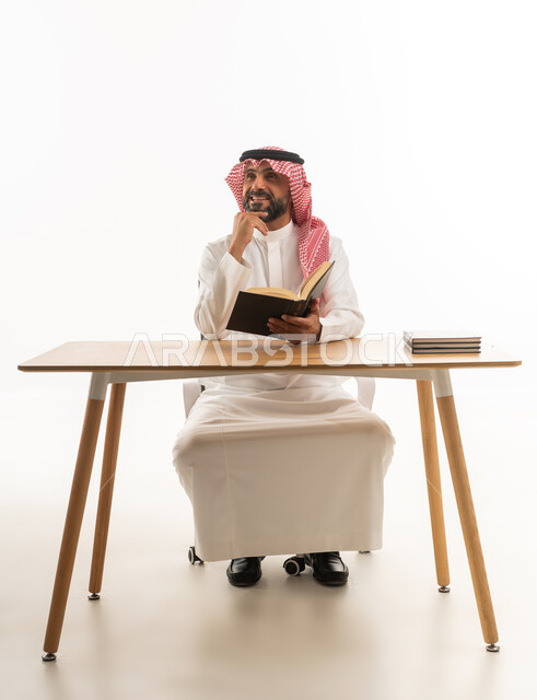 Saudi Man in Traditional Attire Reading at Desk