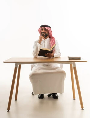 Saudi Man in Traditional Attire Reading at Desk