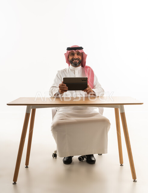 رجل سعودي مع جهاز لوحي على مكتب بخلفية بيضاء