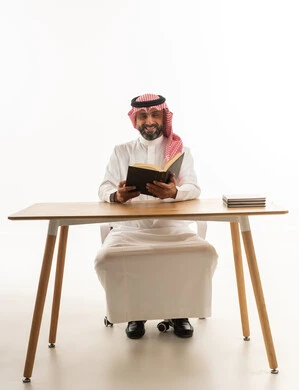 Saudi Man in Traditional Thobe Reading at Office Desk