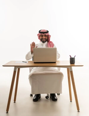 Saudi Man at Desk Waving During Laptop Video Call