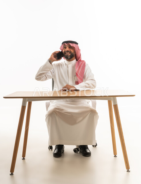 رجل سعودي بالزي التقليدي يتحدث بالهاتف خلف مكتبه