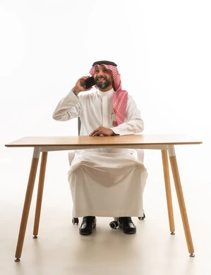 Saudi Man in Traditional Dress Talking on Smartphone at Desk