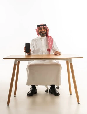 Saudi Man Holding Smartphone at Desk White Background