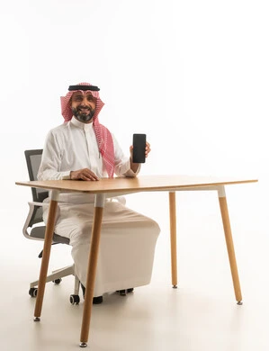 Saudi Businessman at Desk Holding Smartphone on White Background