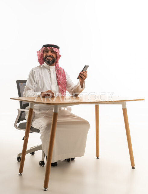Saudi Man in Traditional Dress with Smartphone at Desk