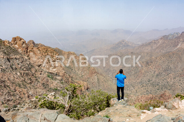 زاوية من الخلف لرجل سائح يقوم بإلتقاط صور لجبال الشفا في مدينة الطائف بالمملكة العربية السعودية ، أماكن سياحية بالسعودية ، جو ضبابي على جبال الطائف ، المرتفعات الجبلية ، مناظر طبيعية جبلية جميلة تقع في مدينة الطائف بالسعودية ، جبال الطائف