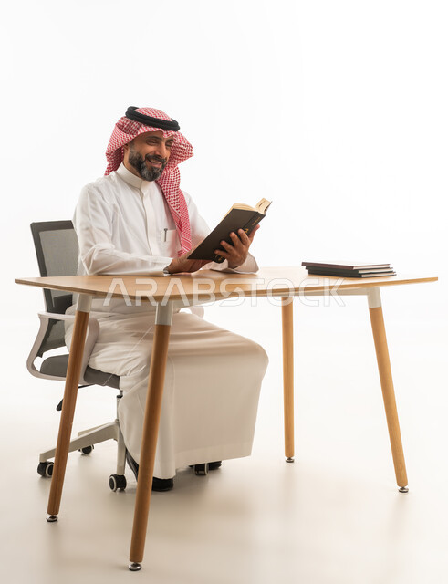 رجل أعمال سعودي يقرأ كتاباً على مكتب عمل