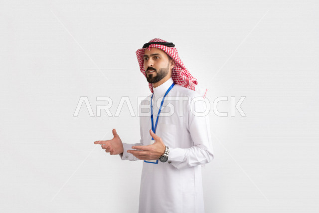 بورتريه مقرب جانبي لرجل عربي خليجي سعودي يرتدي الزي السعودي التقليدي، يضع بطاقة تعريفية بشريط ازرق حول رقبته ويشير بيديه، ايماءات الشرح والتوضيح، محاضرات ودروس جامعيه ، مفهوم مهنه التدريس، خلفيه بيضاء