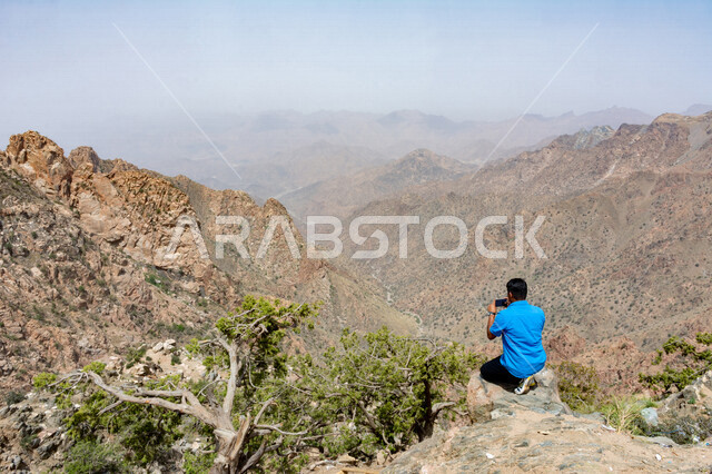 زاوية من الخلف لرجل سائح يقوم بإلتقاط صور لجبال الشفا في مدينة الطائف بالمملكة العربية السعودية ، أماكن سياحية بالسعودية ، جو ضبابي على جبال الطائف ، المرتفعات الجبلية ، مناظر طبيعية جبلية جميلة تقع في مدينة الطائف بالسعودية ، جبال الطائف