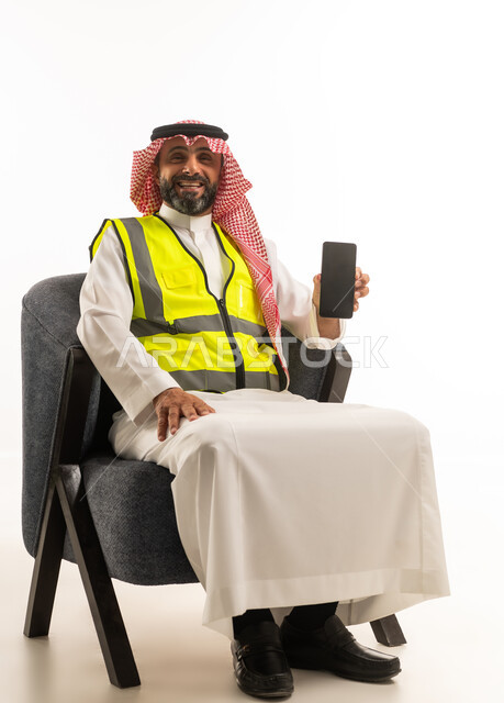 رجل سعودي بسترة سلامة يحمل هاتفاً ذكياً