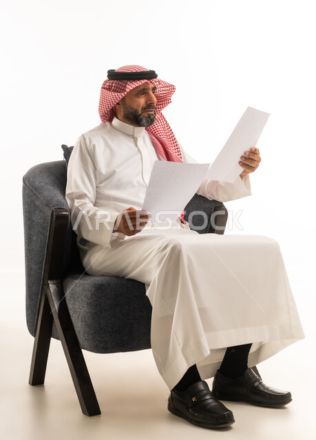 رجل سعودي بالزي التقليدي يراجع أوراق عمل