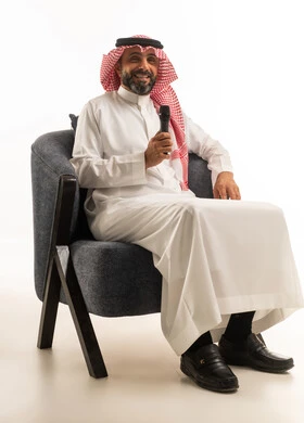 رجل سعودي يمسك ميكروفون جالس على كرسي عصري