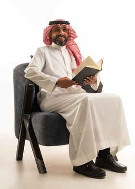 رجل سعودي يجلس على كرسي ويقرأ كتاباً