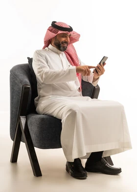 Saudi Man in Thobe Using Smartphone in Armchair