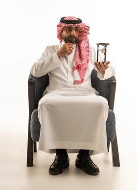 رجل سعودي يحمل ساعة رملية على خلفية بيضاء