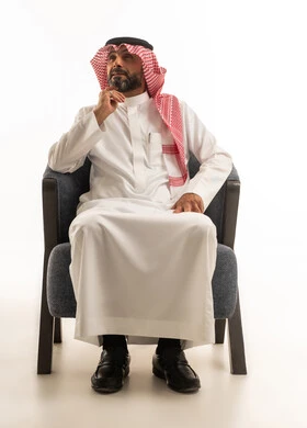 رجل سعودي بالزي التقليدي في وضعية تفكير على كرسي