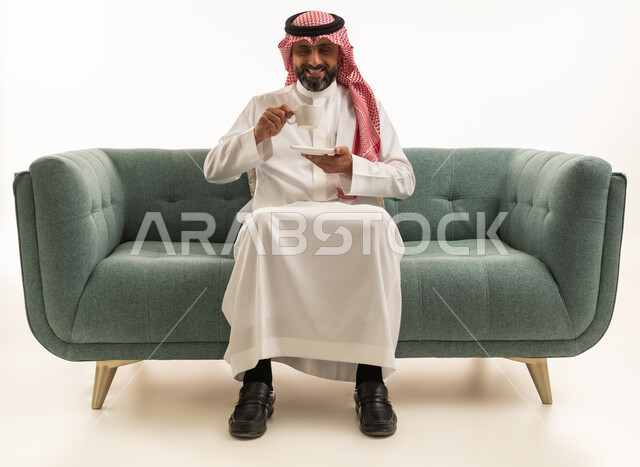 رجل سعودي بالزي التقليدي يشرب القهوة على الأريكة