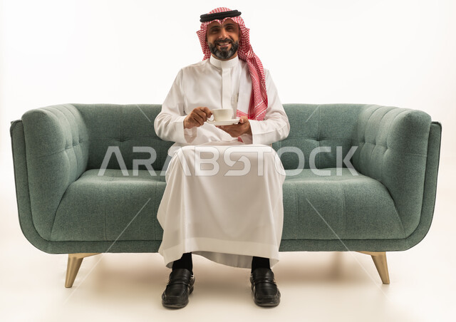 رجل سعودي بالزي التقليدي يجلس على الأريكة مع قهوة